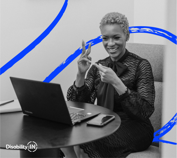A smiling woman faces her laptop screen and communicates over video using sign language.